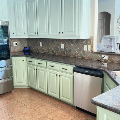 A finished kitchen with cabinets repainted sage green by JC Painting Services, against a stone tile backsplash and granite counters