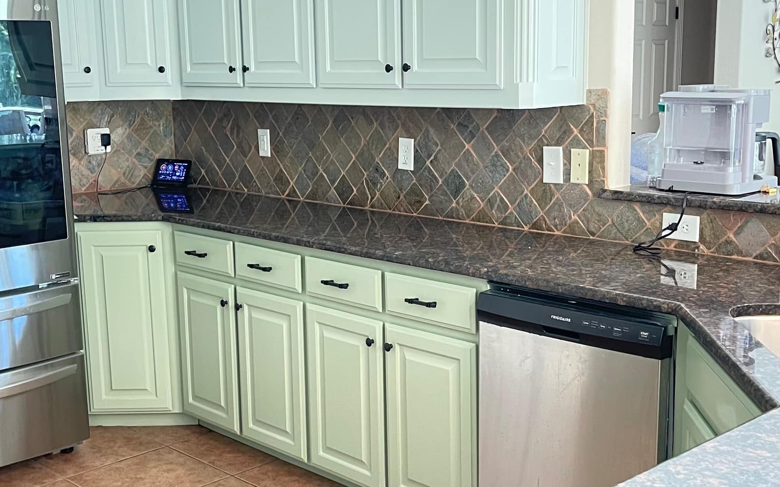 A finished kitchen with cabinets repainted sage green by JC Painting Services, against a stone tile backsplash and granite counters
