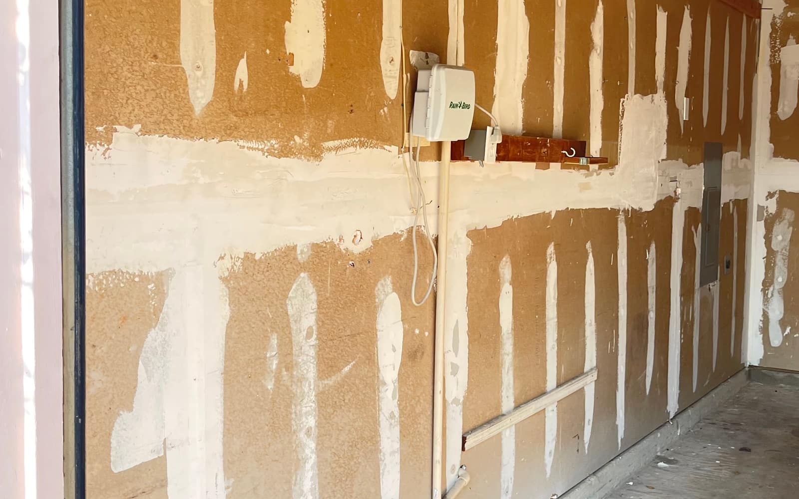 A garage wall mid-repair by JC Painting Services, with joint compound worked over the drywall seams and screw lines ready for sanding