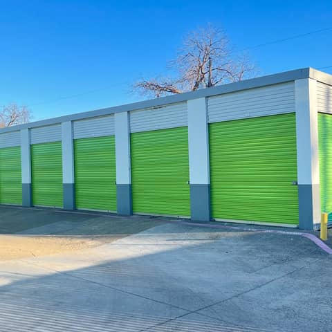 A row of commercial roll-up doors freshly repainted bright green by JC Painting Services, under a clear Texas sky