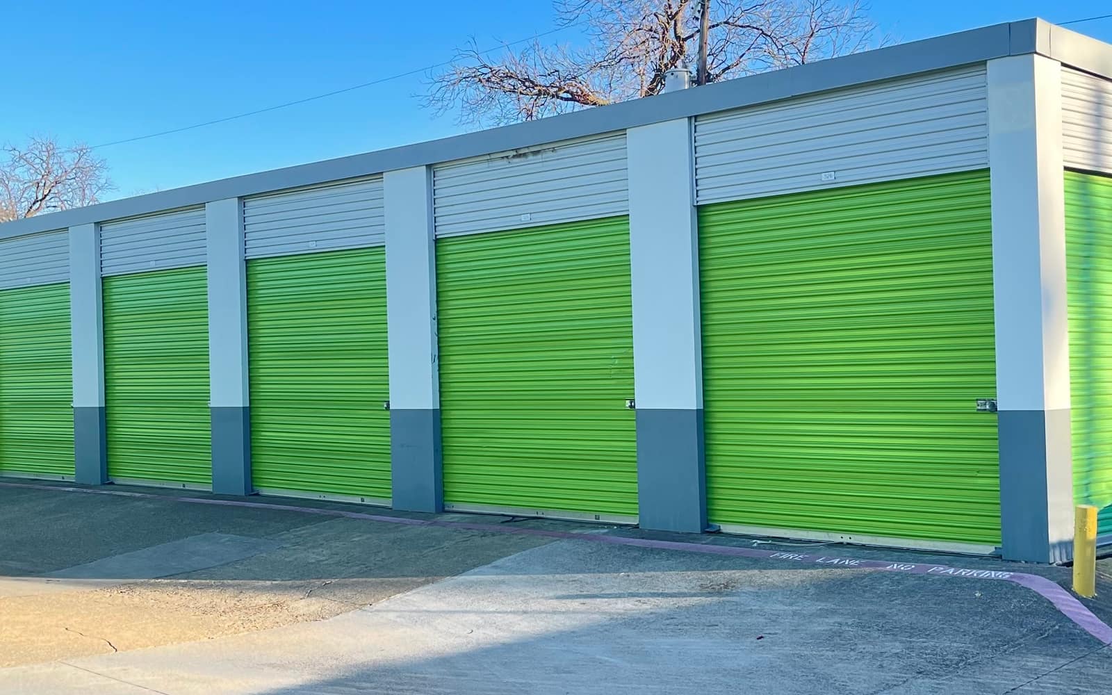 A row of commercial roll-up doors freshly repainted bright green by JC Painting Services, under a clear Texas sky